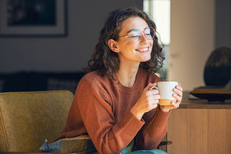 A woman sitting and smiling while holding a cup of coffee.