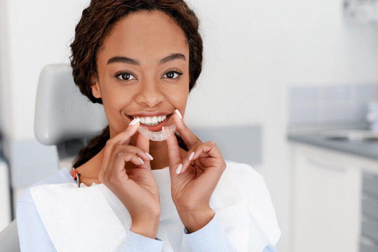 A patient sits in a dental chair wearing a bib and holding a clear aligners, preparing for a procedure in a modern clinic. The setting suggests a consultation or treatment related to dental implants and oral care.